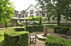 Das Spital-Gebäude von der Rückseite mit einem kleinen angelegten Parkt mit Bäumen und Buchsbaumhecken und Sitzgelegenheiten 